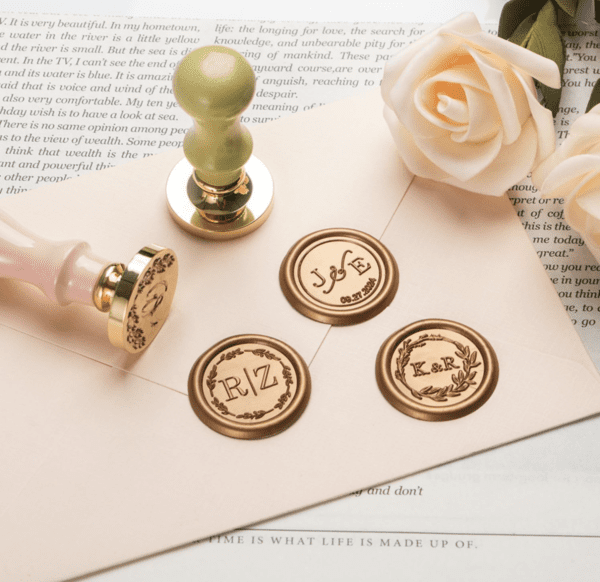 Two decorative wax seals and stamps in pink and green, arranged on a light paper background with a cream rose.